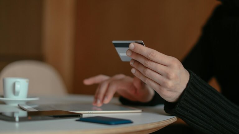 A person studies a credit or debit card while using a tablet device. (Cup of Couple / Pexels.com)