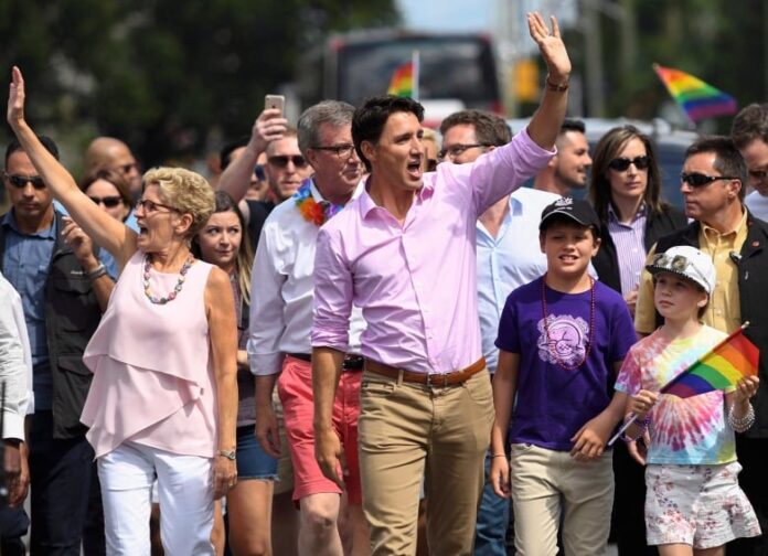 A group of people marching down a street with gay pride flags; mostly adults, but also two children.