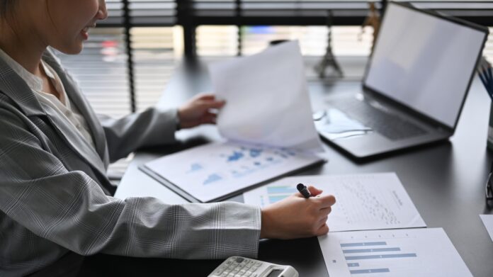 How to Hire a Marketing Director Concentrated female director reviewing financial charts and graphs data in document at office desk.