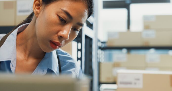 Woman wear formal shirt hold digital tablet check inventory online stock data in cardboard box.