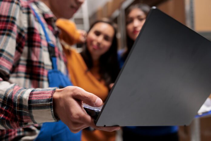 Warehouse manager showing coworkers inventory software on laptop