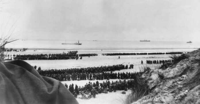 A black and white photo shows thousands of soldiers on a French beach waiting to be evacuated to England.